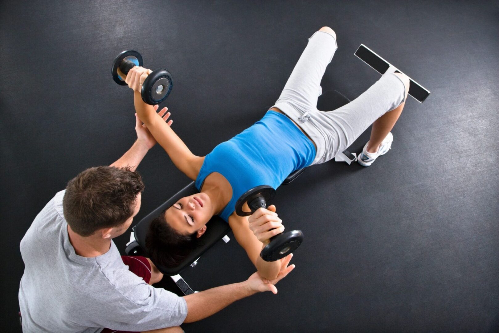 A woman is lying on the ground while another man holds two dumbbells.